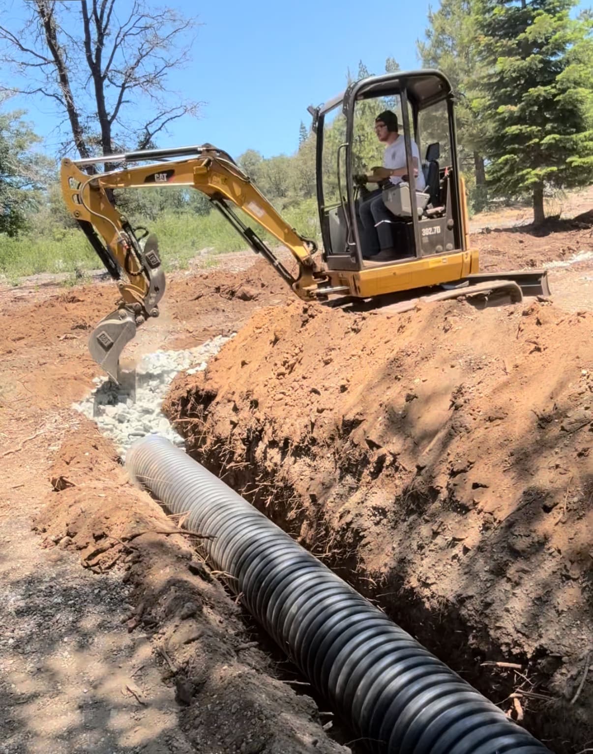 Calterra excavator installing drainage on a wooded property